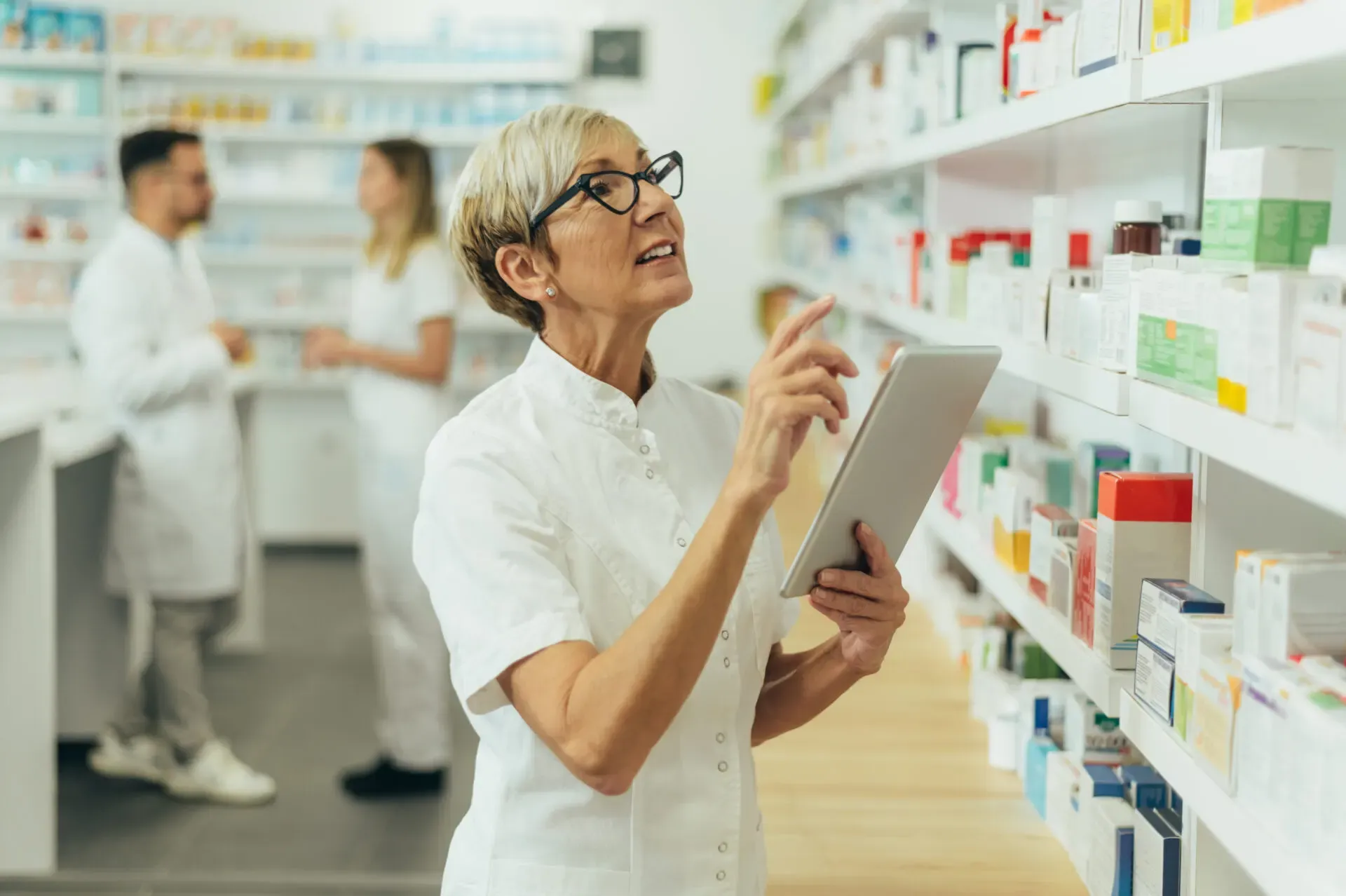 Pharmacist using a digital tablet to check stock in the pharmacy aisle, Pan Pharmacy – Common lane