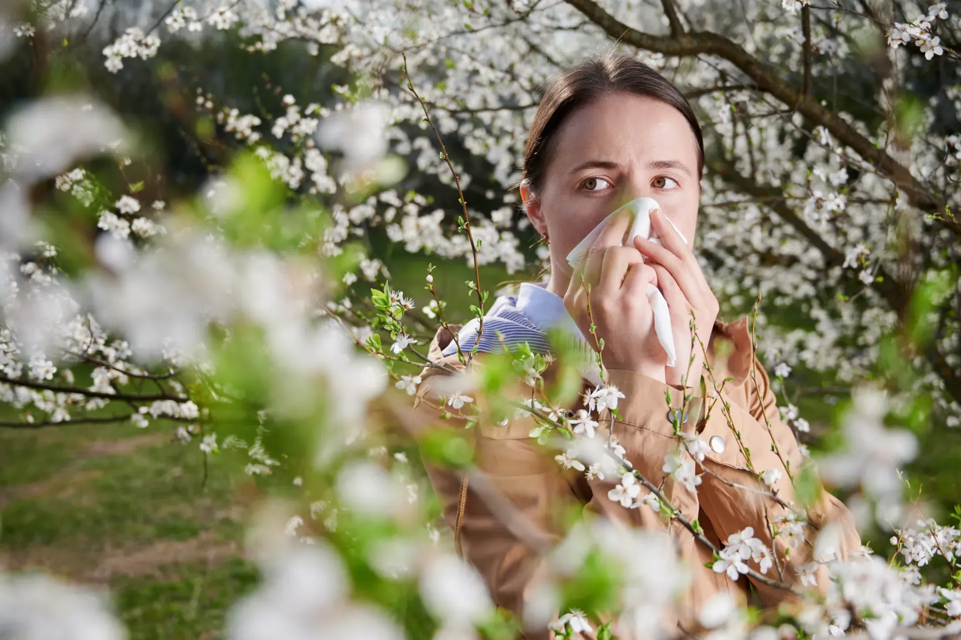 Woman sneezing from hay fever in a spring garden