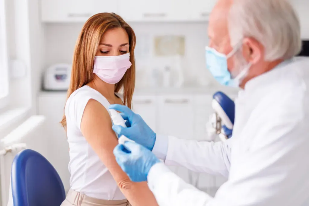 Woman in a face mask having her arm prepared for a Covid vaccination at Pan Pharmacy Birmingham